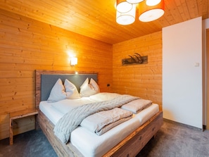 A wooden-paneled bedroom with a bed, bedside table, and wall-mounted light fixture. - Modern Apartment in Kitzbuhel Near Ski Area (Kitzbuhel)