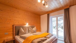 A wooden-paneled bedroom with a bed, a nightstand, and a window with curtains. - Modern Apartment in Kitzbuhel Near Ski Area (Kitzbuhel)