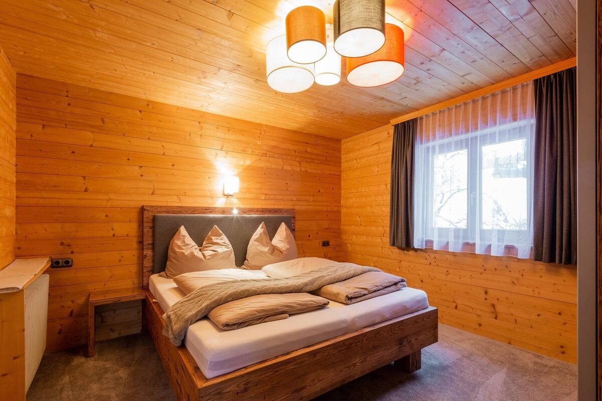 Ett sovrum i en stuga med träpanel, inrett med en säng, ett nattduksbord och ett fönster med gardiner.