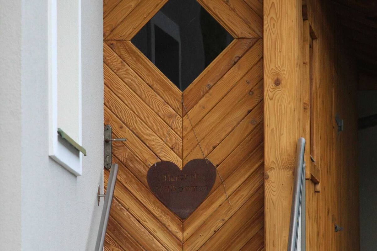 En dörr av trä med ett hjärtformat utskuret mönster och ett fönster ovanför.