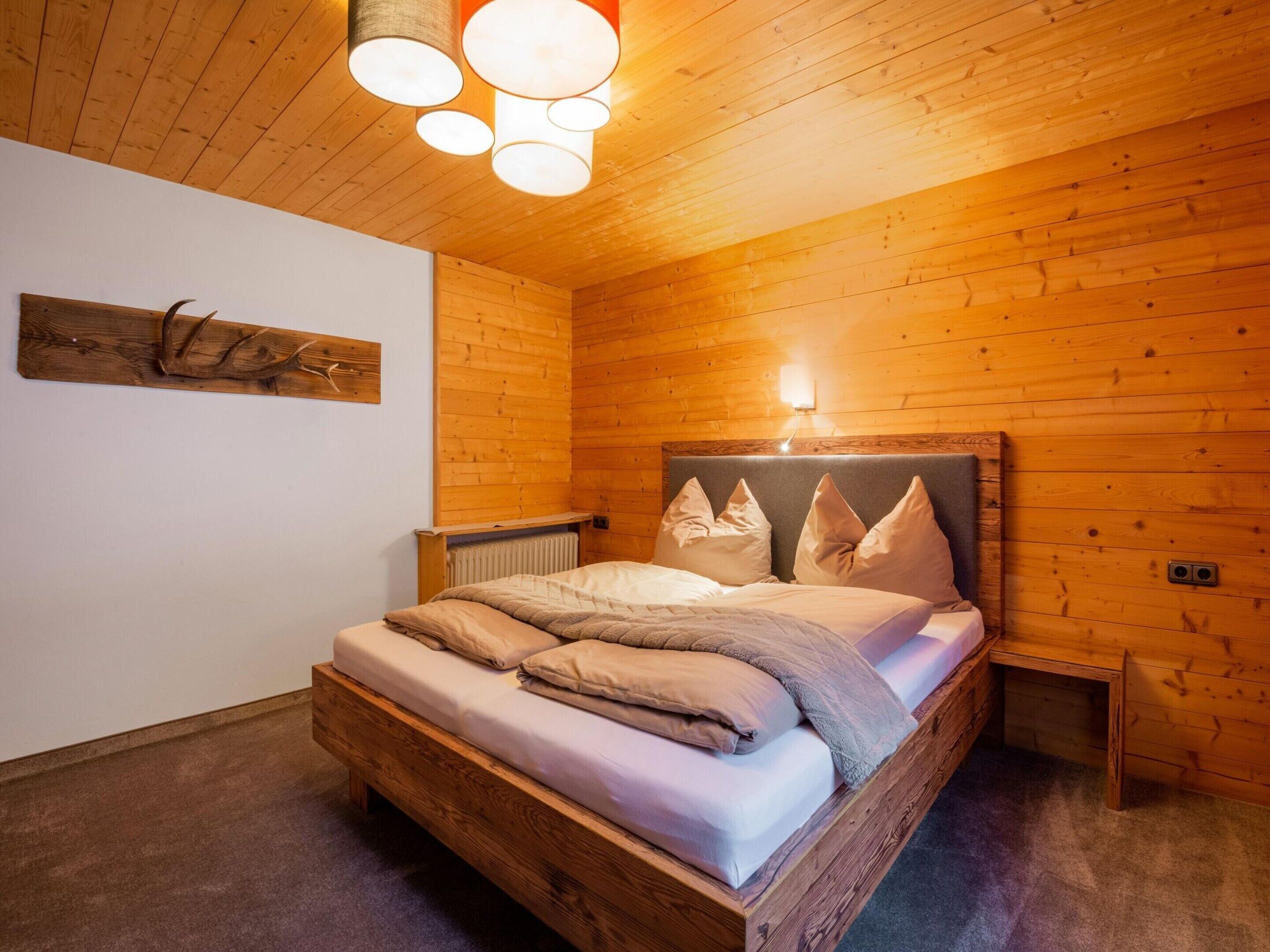 A wooden-paneled room with a bed, a wall-mounted light fixture, and a radiator.