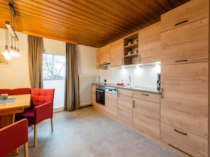 A modern kitchen with wooden cabinets, a built-in oven, and a dining area with red chairs. - Modern Apartment in Kitzbuhel Near Ski Area (Kitzbuhel)