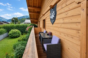 A wooden deck with a table and chairs, surrounded by greenery and a mountain view. - Modern Apartment in Kitzbuhel Near Ski Area (Kitzbuhel)
