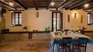 A rustic dining area with exposed wooden beams, a brick floor, and a table set for two with a blue tablecloth. - Gorgeous Apartment With Pool Near Sibillini Mountains (Monte San Martino)