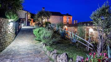 A stone pathway leading to a stone building with a wooden fence and greenery.