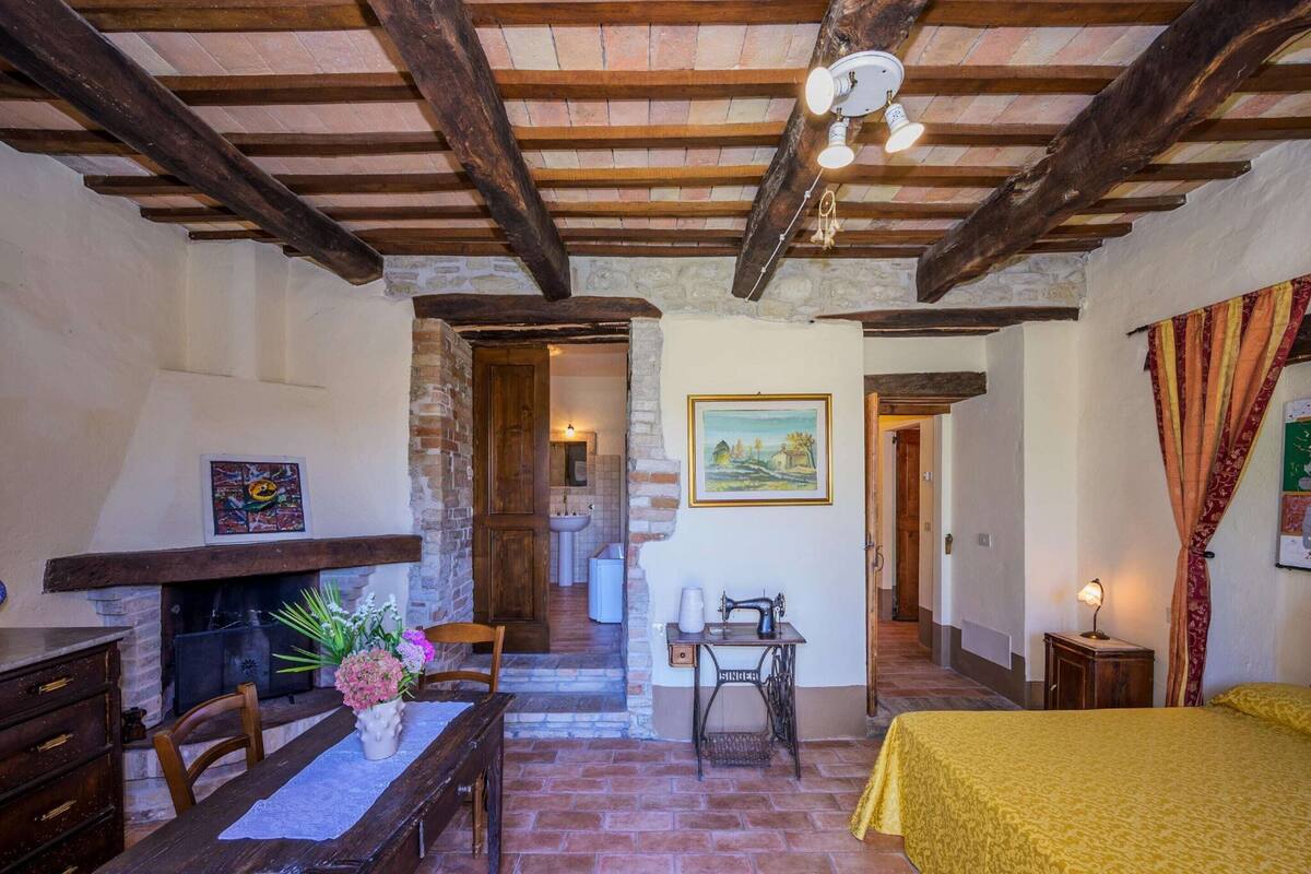 A rustic room with a wooden table, a bed with a yellow bedspread, a sewing machine, and a fireplace.