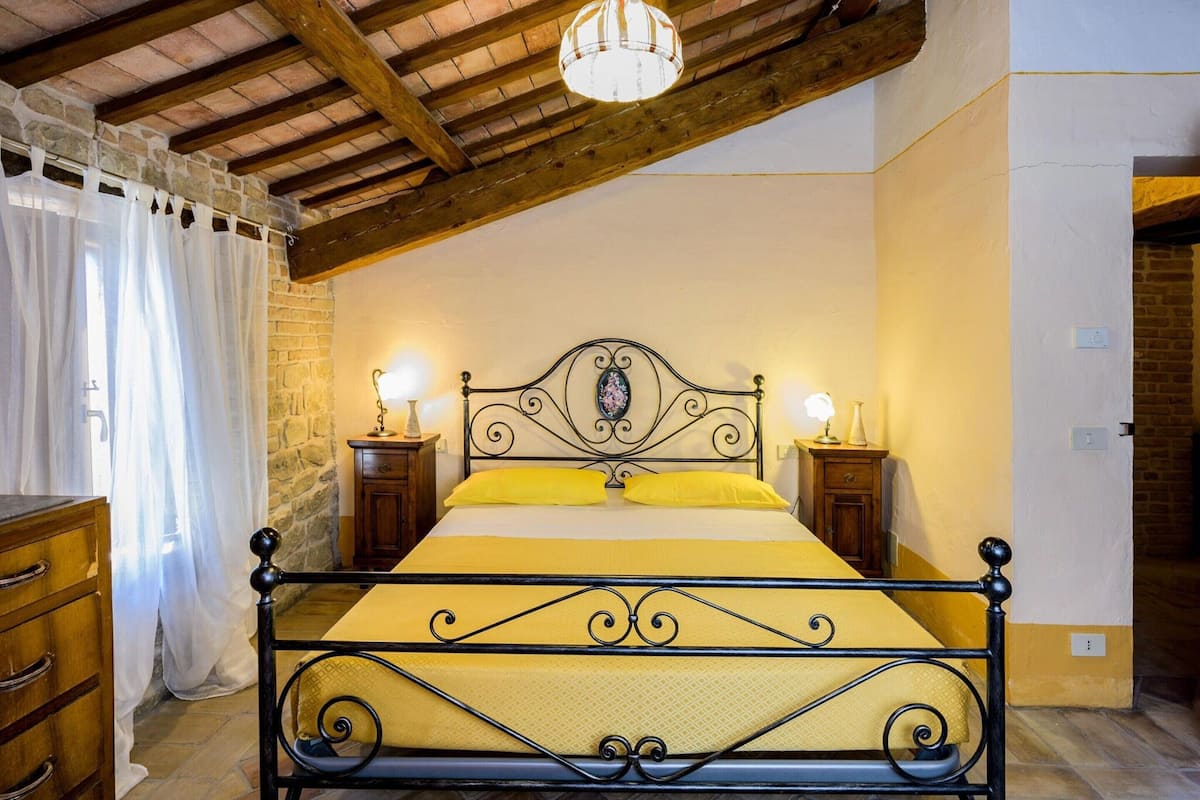A bedroom with a bed, two bedside tables, a chandelier, and a wooden ceiling.