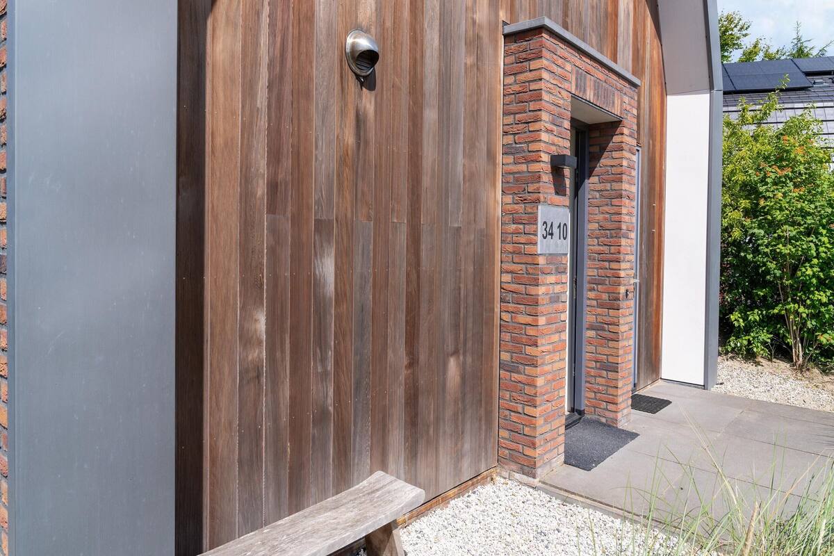 Pared exterior de madera con una puerta metálica y un acceso de ladrillo.