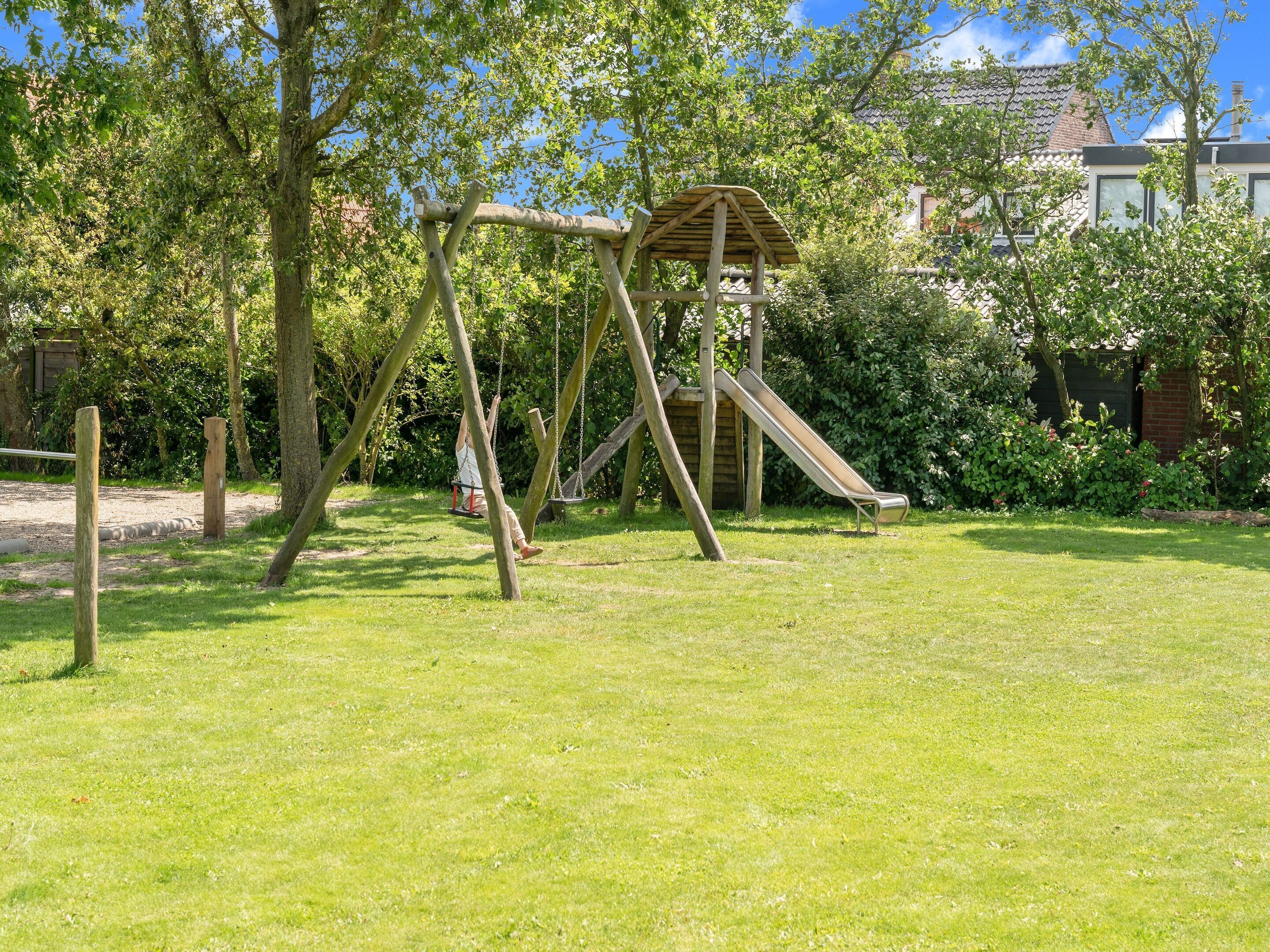 Un'area giochi con altalene e uno scivolo, circondata da alberi e un prato.