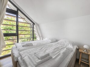 A bedroom with a bed, white linens, a wooden nightstand, and a window with curtains.