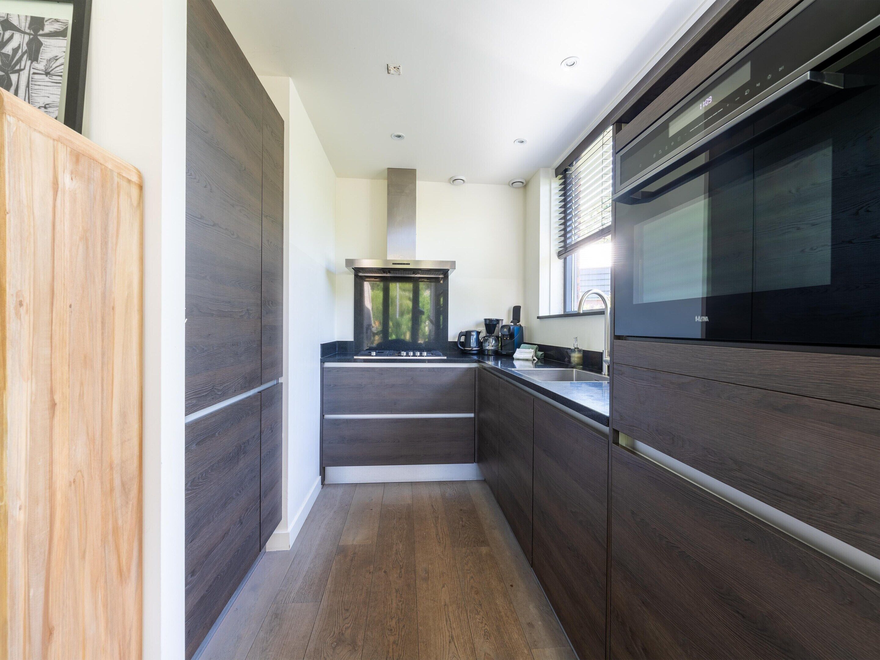 A modern kitchen with dark wood cabinetry, a stainless steel range hood, and a built-in oven.