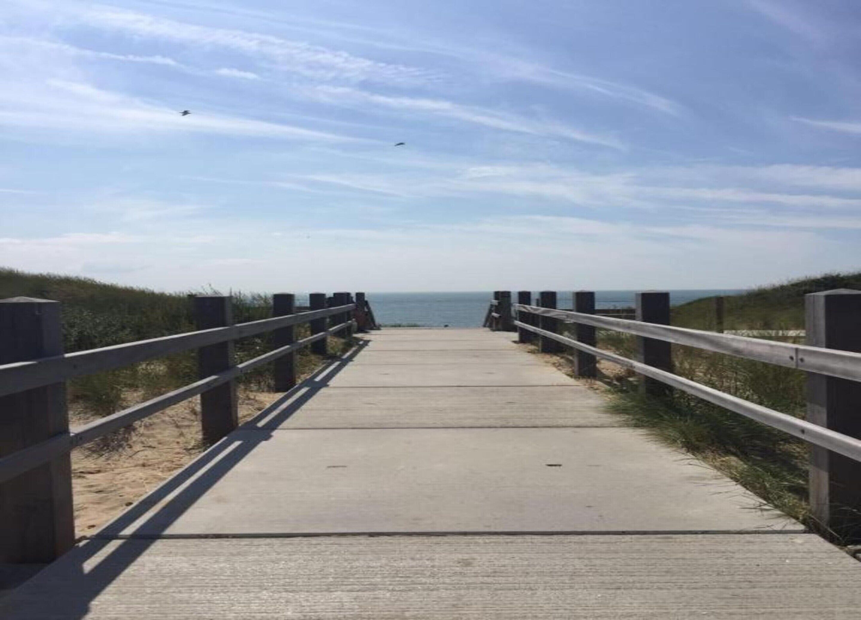 Une promenade en bois menant à la plage, avec des garde-corps de chaque côté.