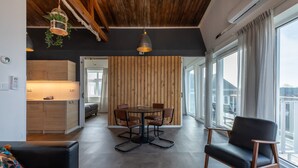 Et moderne interiør med et spiseområde, en sort lædersofa og udsigt gennem store vinduer.