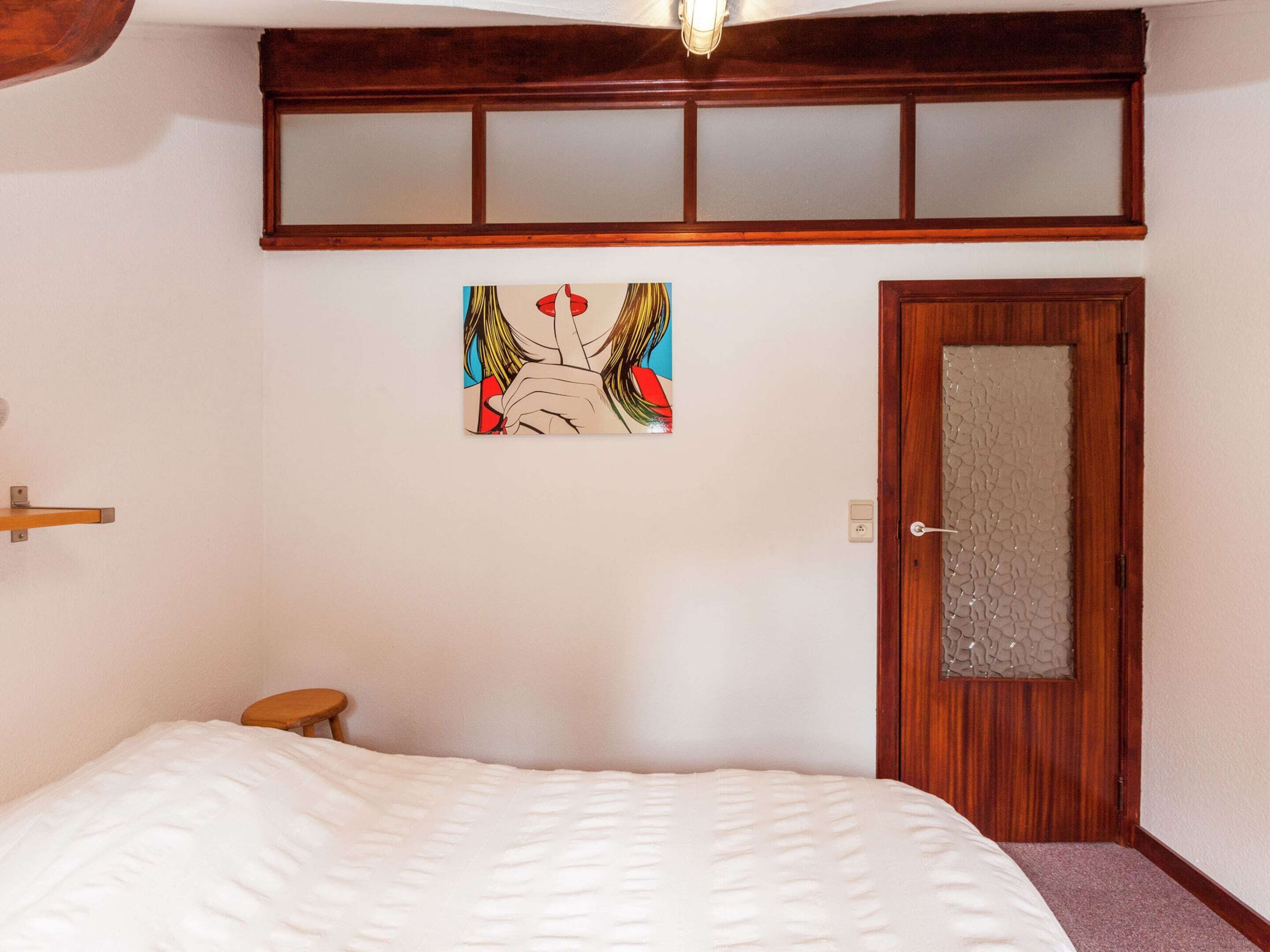 A bedroom with a bed, a wooden door, and a painting on the wall.