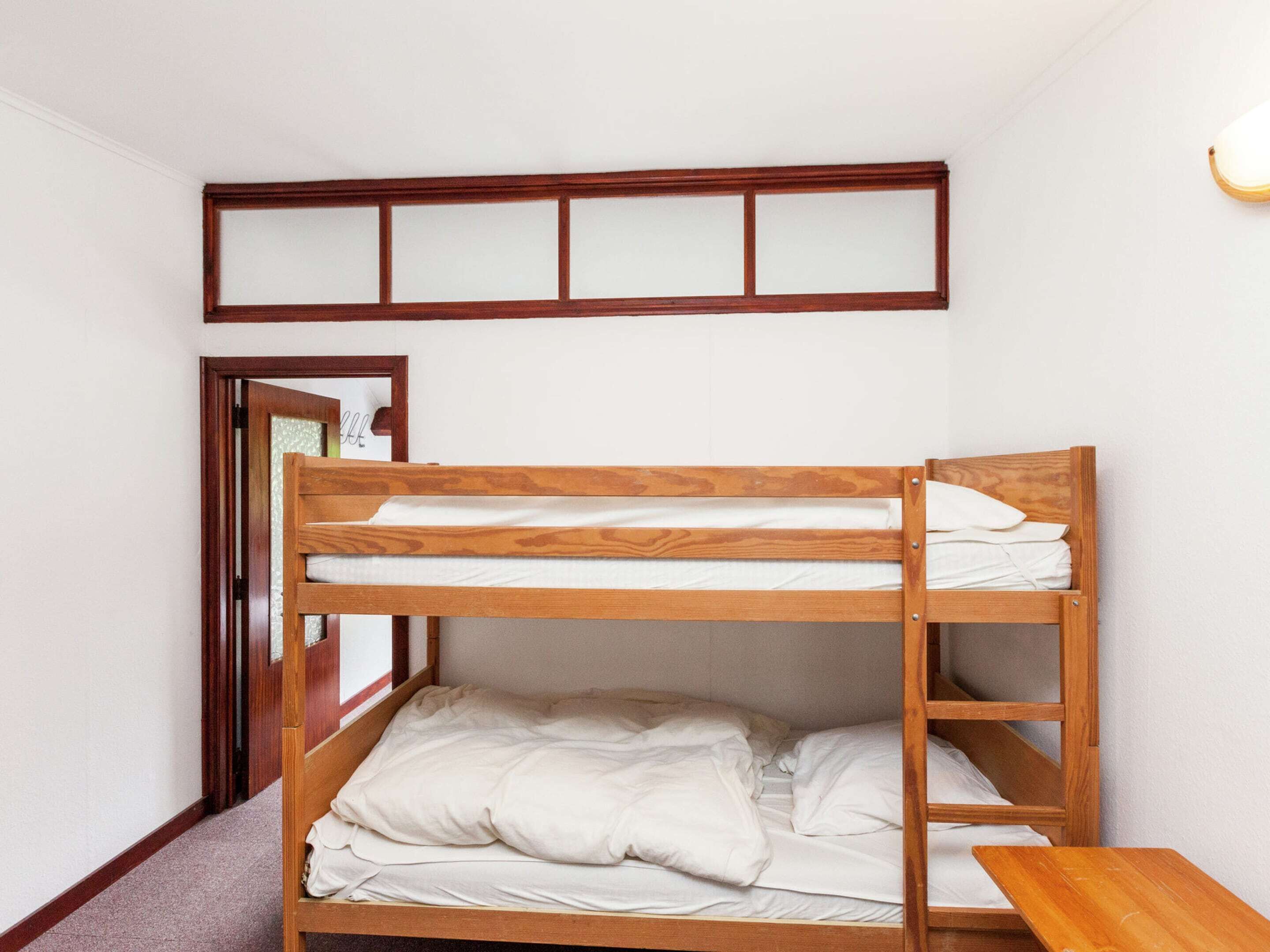 A bunk bed with a wooden frame and white bedding in a room with white walls and a wooden door frame.
