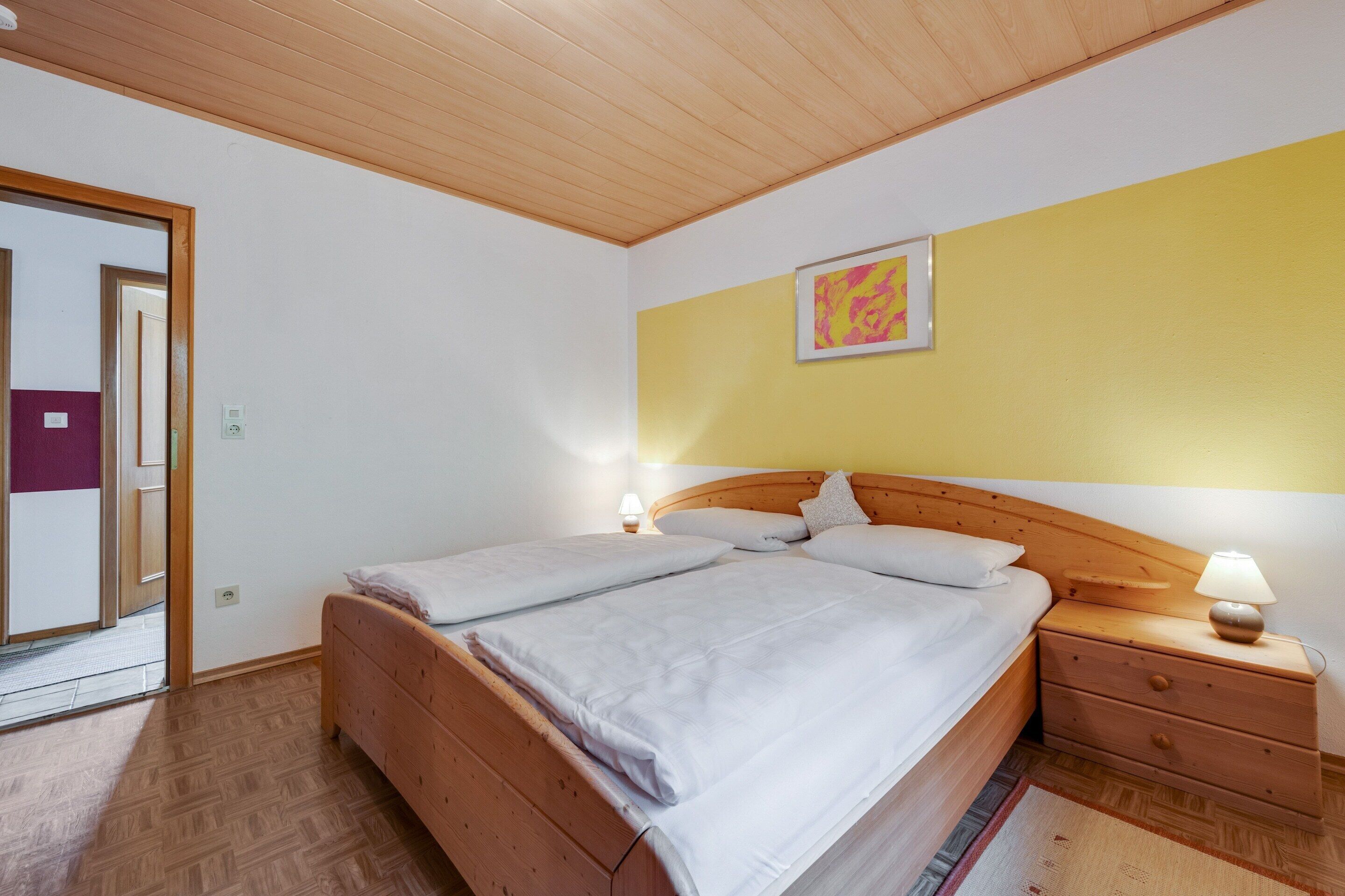 A bedroom with a wooden bed, a nightstand with a lamp, and a painting on the wall.