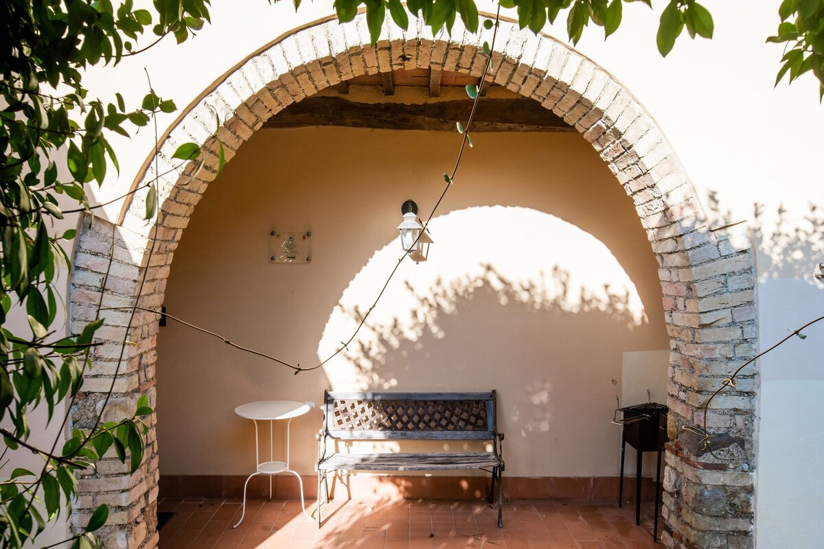 An arched brick structure with a bench, a small table, and a hanging light fixture.