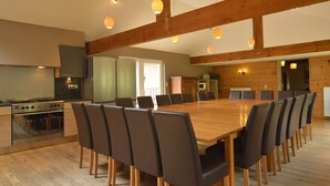A spacious dining area with a long wooden table and multiple chairs, a kitchen with modern appliances, and wooden beams on the ceiling. - Lovely House With Much Luxury and Comfort (Waimes)