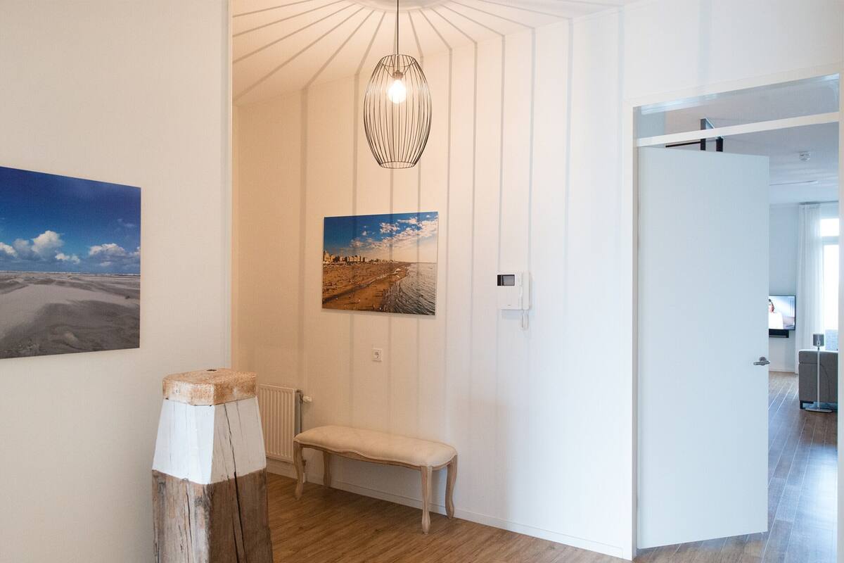 A hallway with wooden flooring, a bench, a hanging light fixture, and two framed pictures on the wall.
