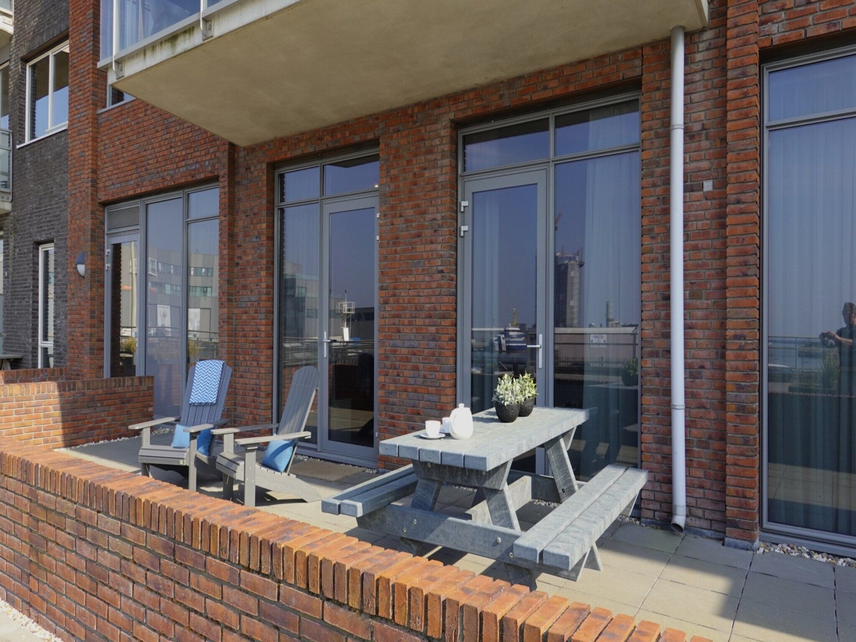 A patio with a table and chairs, a brick wall, and large windows.
