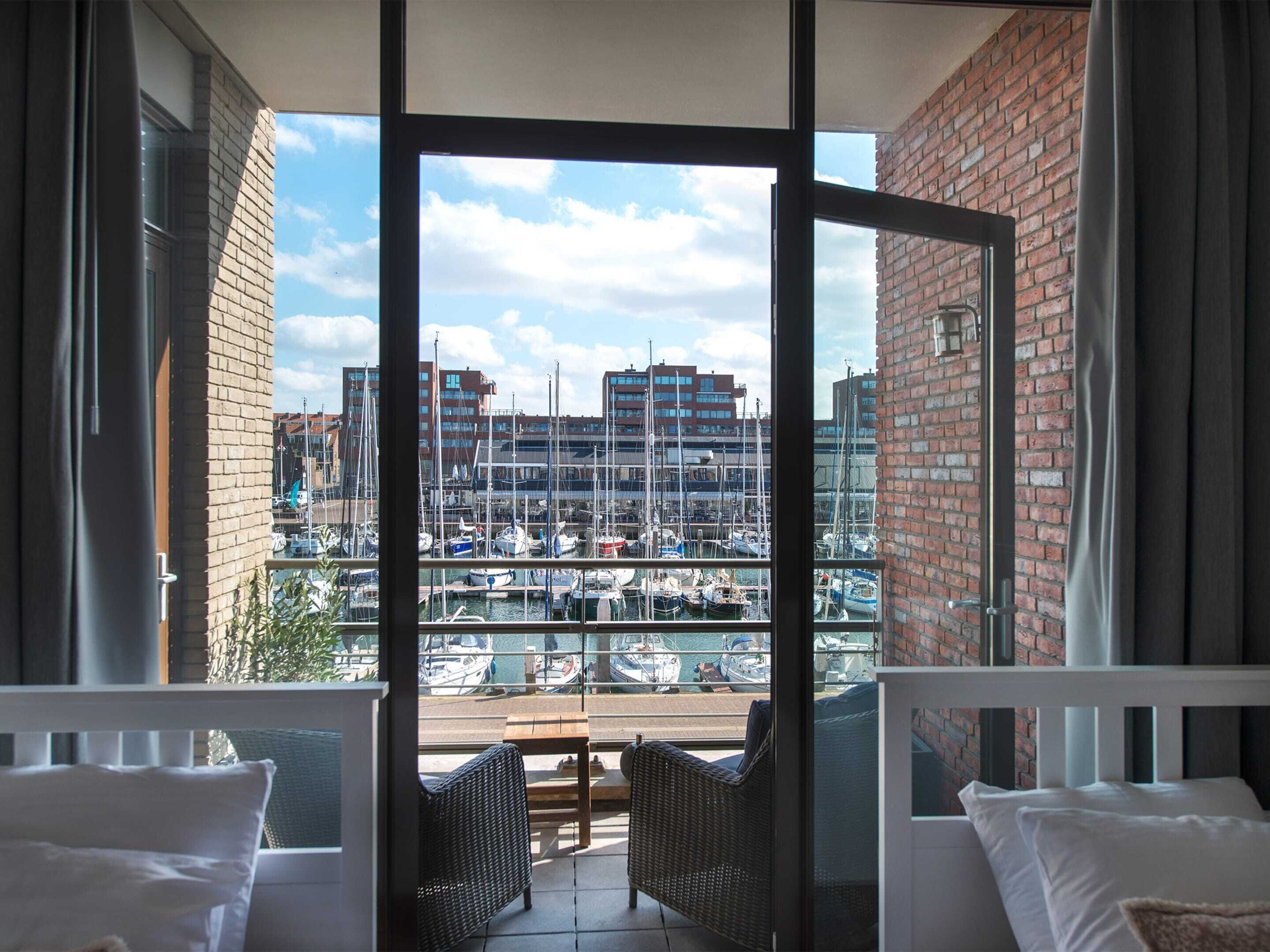 Un balcon agrémenté de meubles en osier, une vue sur une marina avec des bateaux, et un bâtiment en briques en arrière-plan.