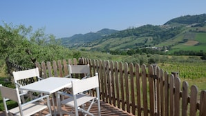 An outdoor patio with a table and chairs, surrounded by a wooden fence, overlooking a hilly landscape. - Lovely Holiday Home in Monte Colombo on Farm (Montescudo)