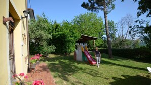 A residential area with a brick pathway, a small garden with pink flowers, and a colorful slide structure. - Lovely Holiday Home in Monte Colombo on Farm (Montescudo)