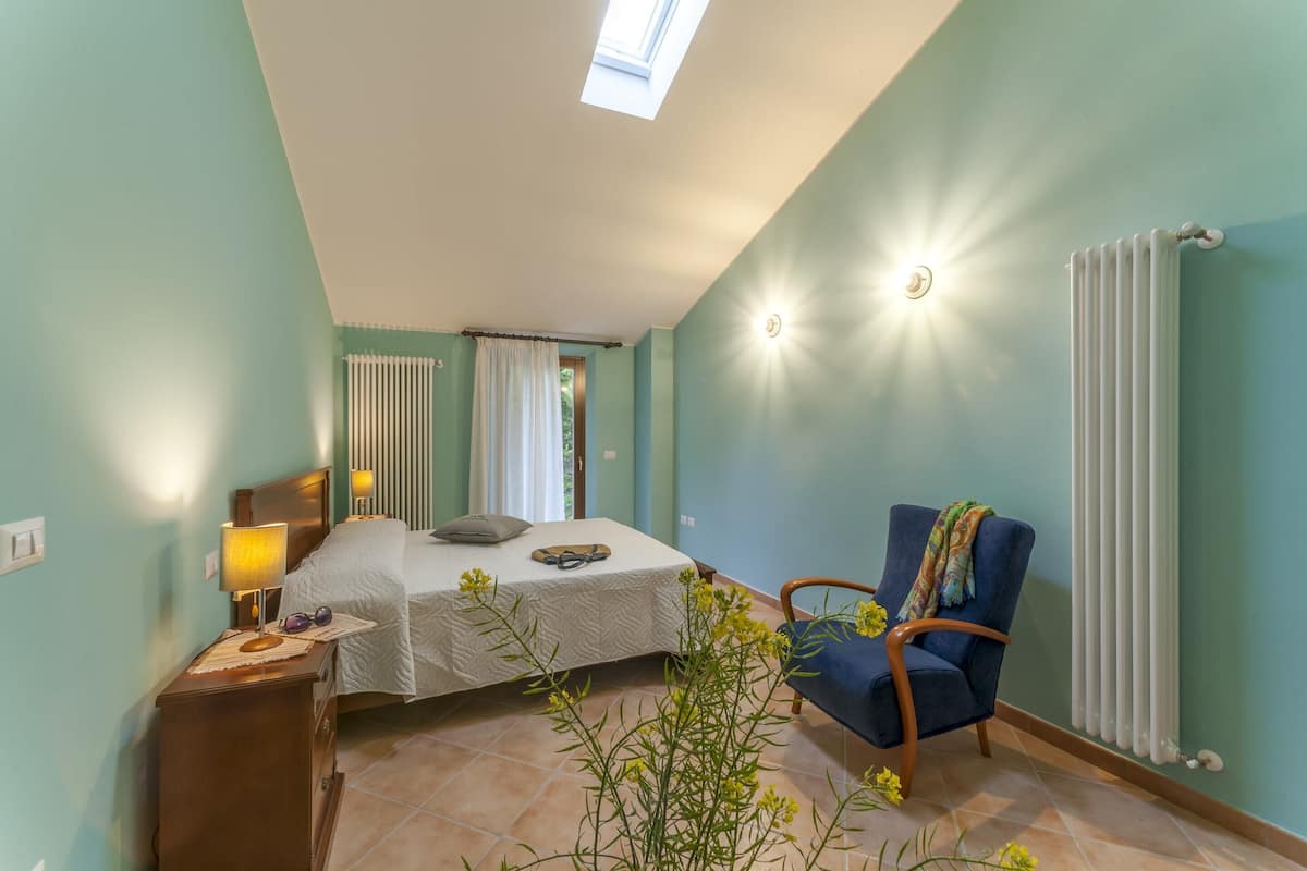 A bedroom with a bed, a chair, a lamp, a radiator, and a window.