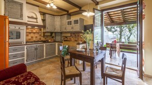 A kitchen with wooden cabinets, a dining table with chairs, and a view of the outdoors through a glass door. - Inviting Holiday Home in San Costanzo With Swimming Pool (San Costanzo)