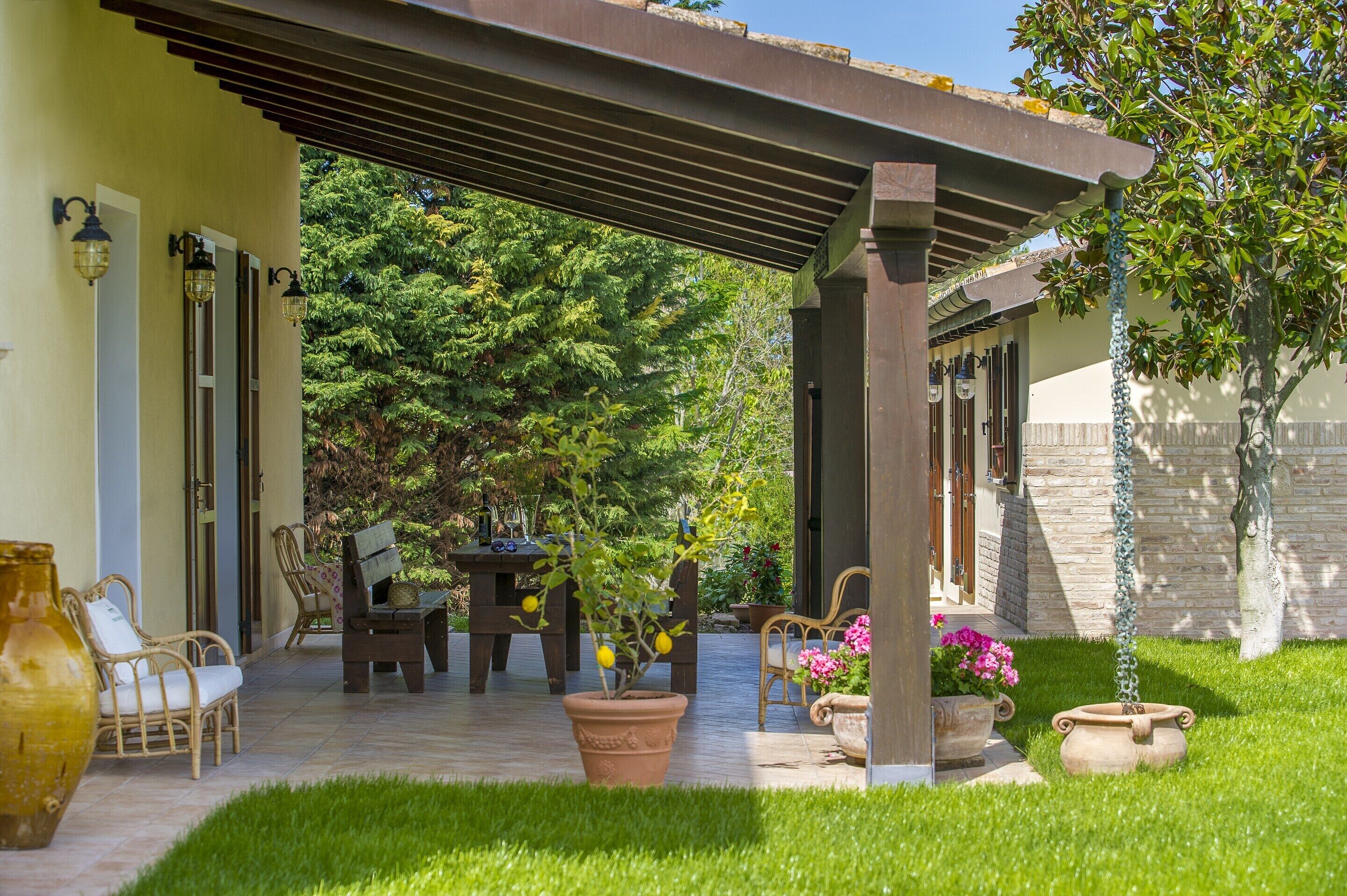 A covered patio area with outdoor furniture, potted plants, and a pergola structure.