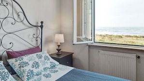 A bedroom with a bed, a nightstand, a lamp, and a window with a view of the beach. - Amazing Holiday Home Near Pet-friendly Beach (Carrara)