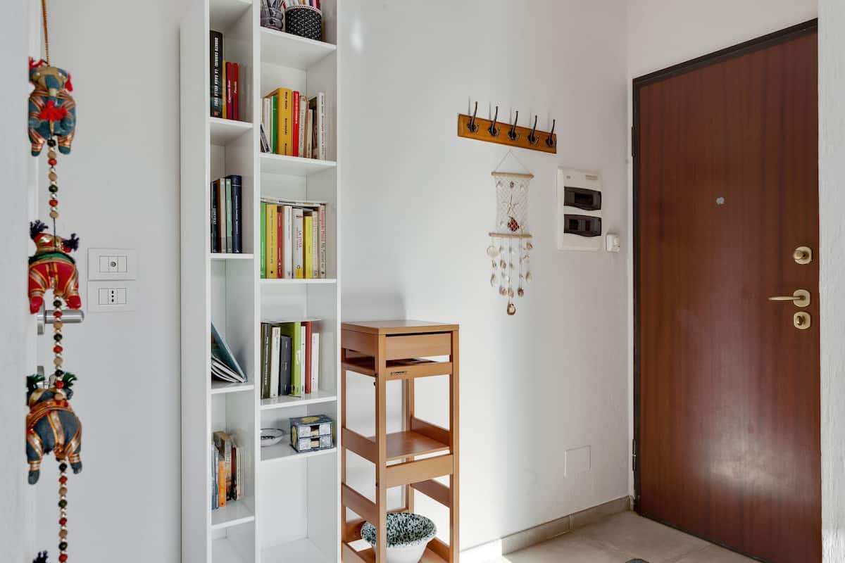 Una habitación con una estantería blanca, una mesita de madera, una puerta y ganchos en la pared.