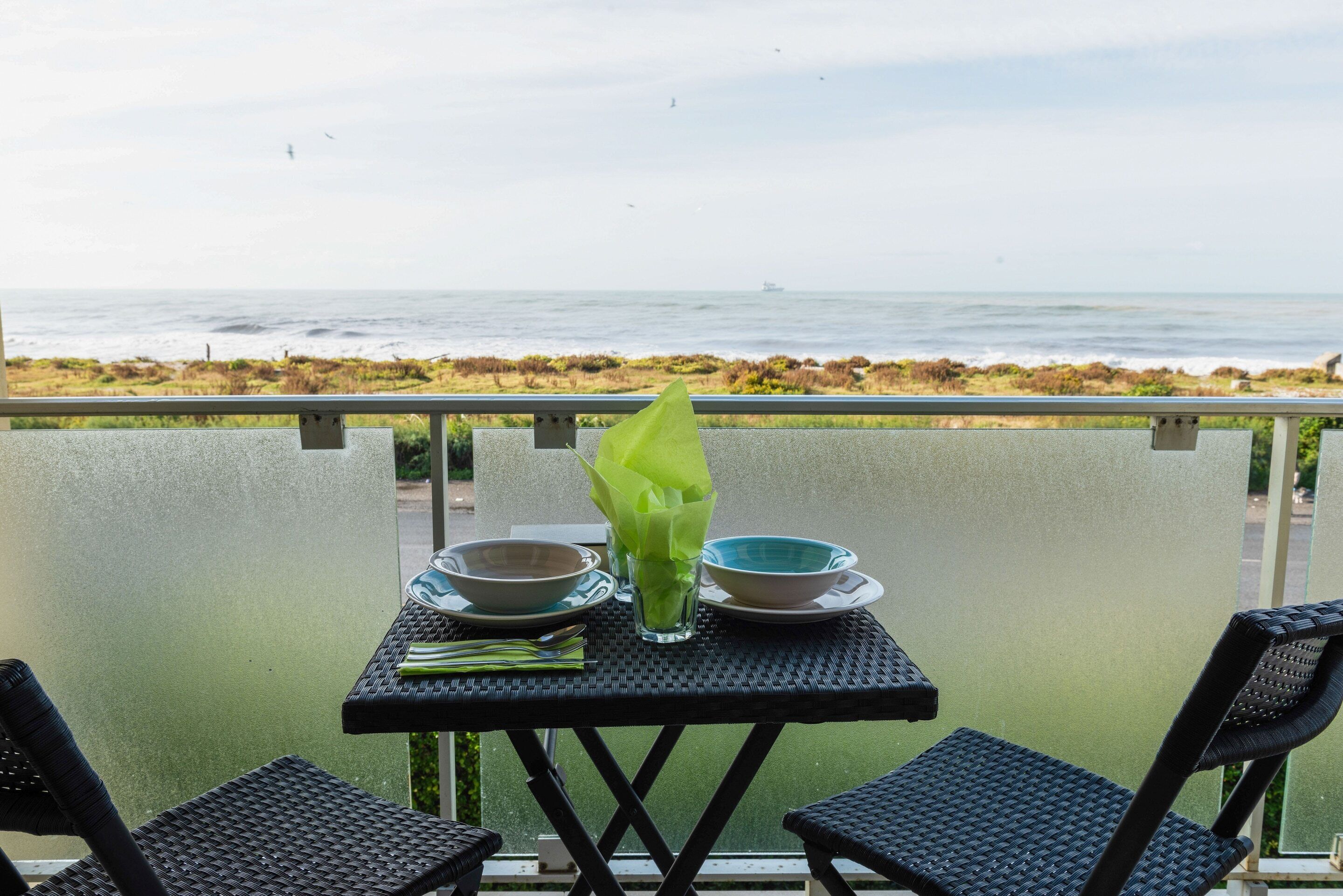 A table with two bowls and a glass of green drink on a balcony overlooking the ocean.