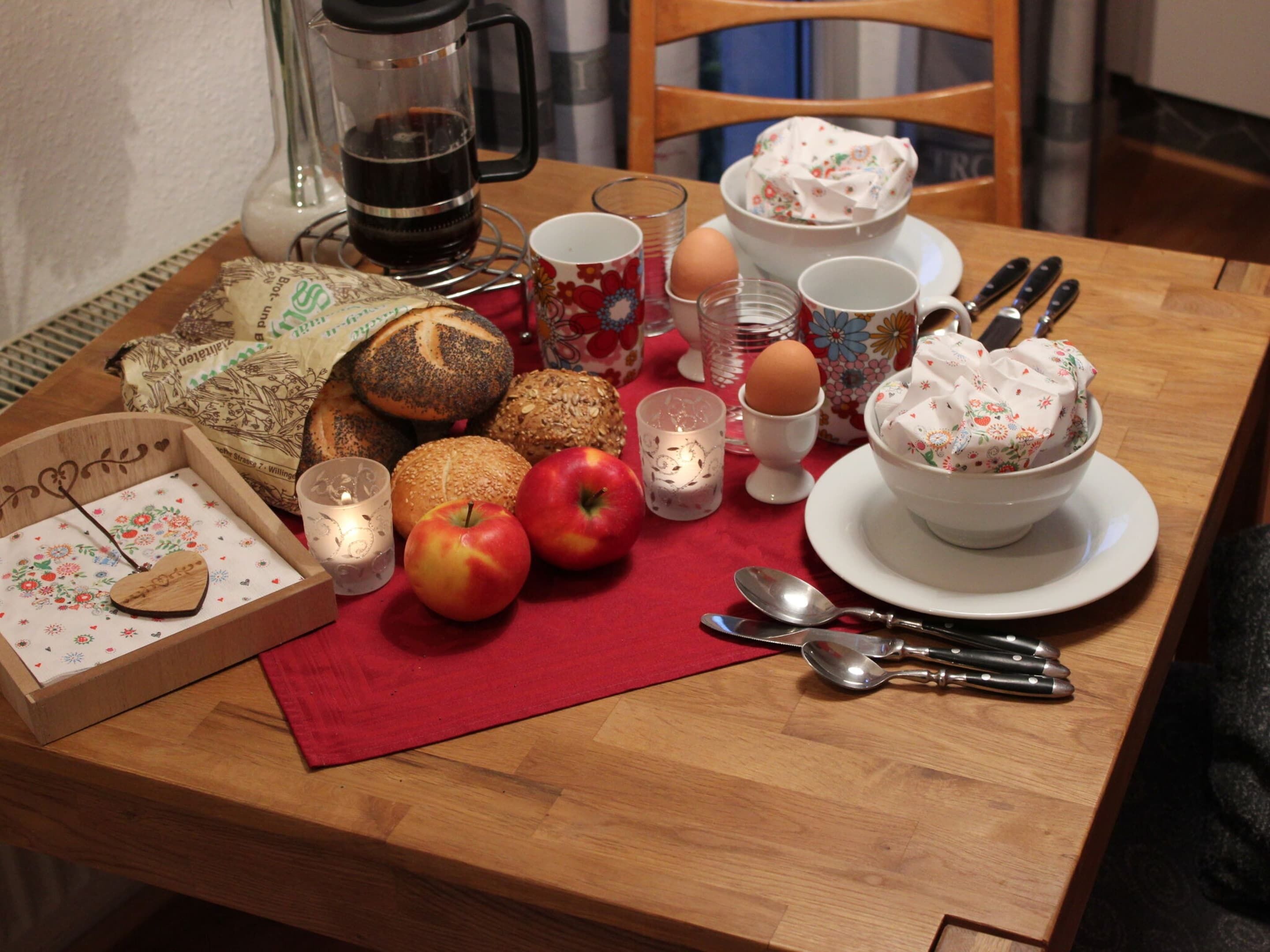 A breakfast table with bread, eggs, apples, and a coffee maker.