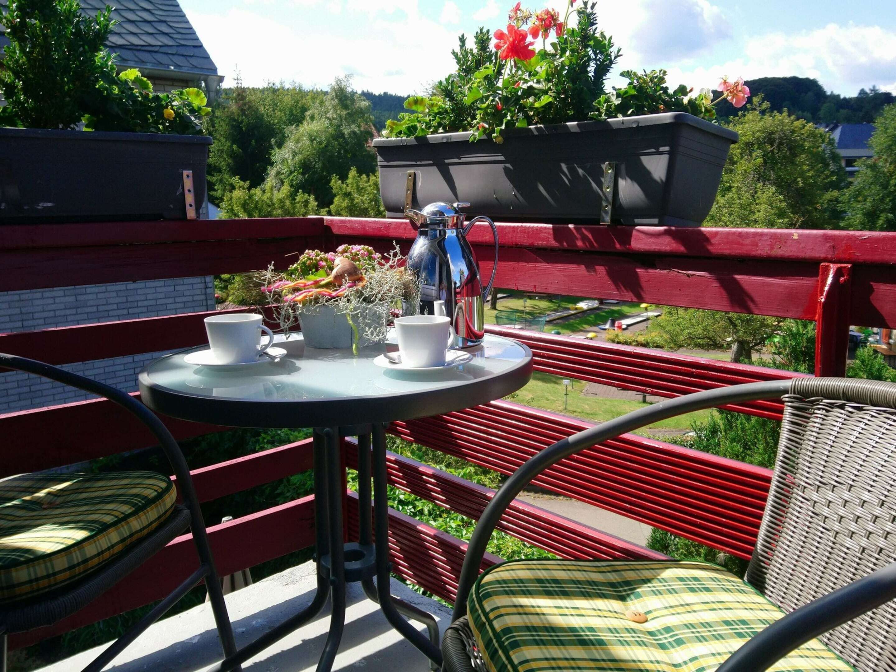A balcony with a table, chairs, and potted plants.