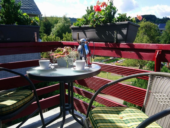 A balcony with a table, chairs, and potted plants.