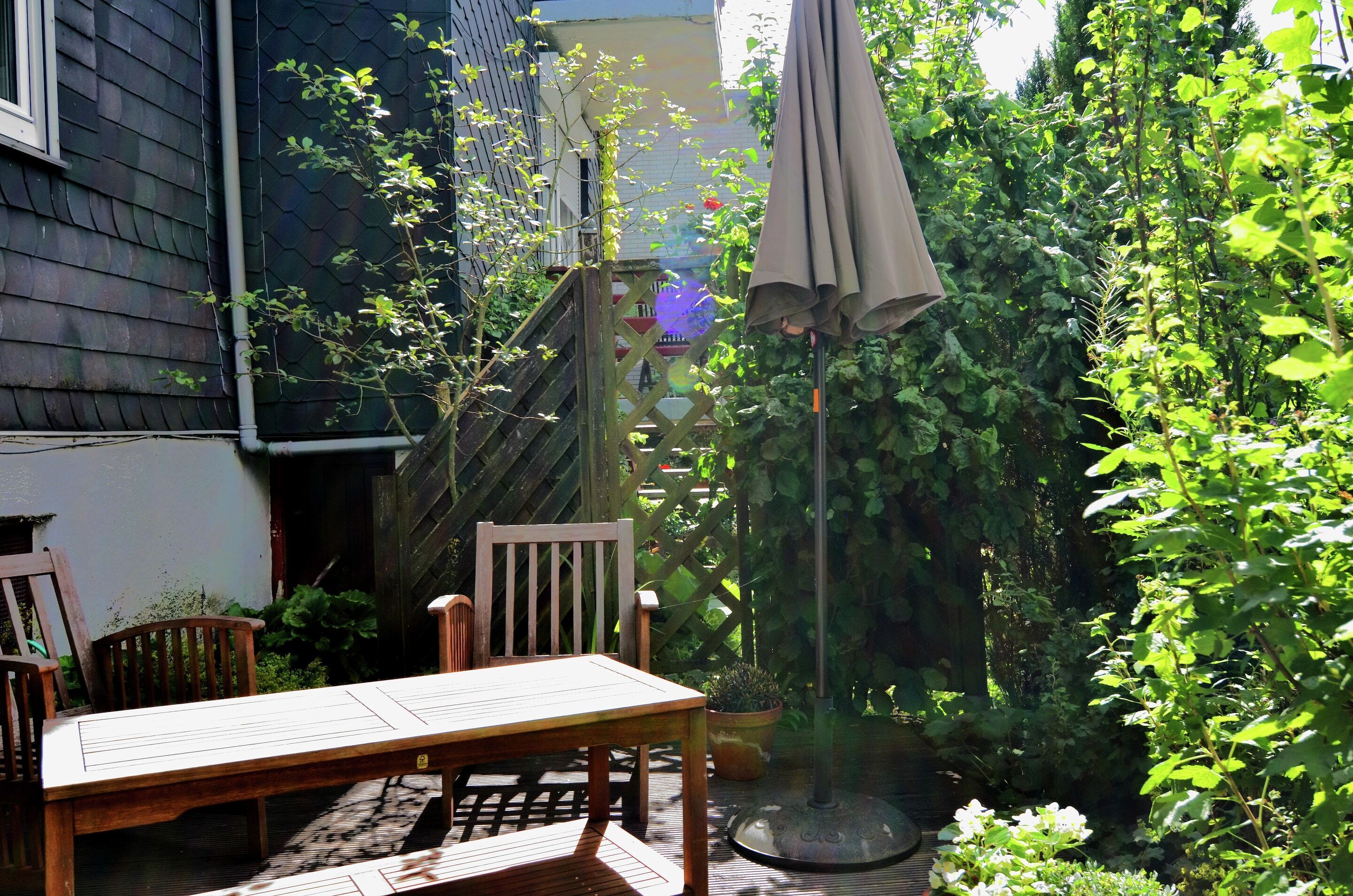 A wooden table and chairs in a garden area with a pergola and potted plants.