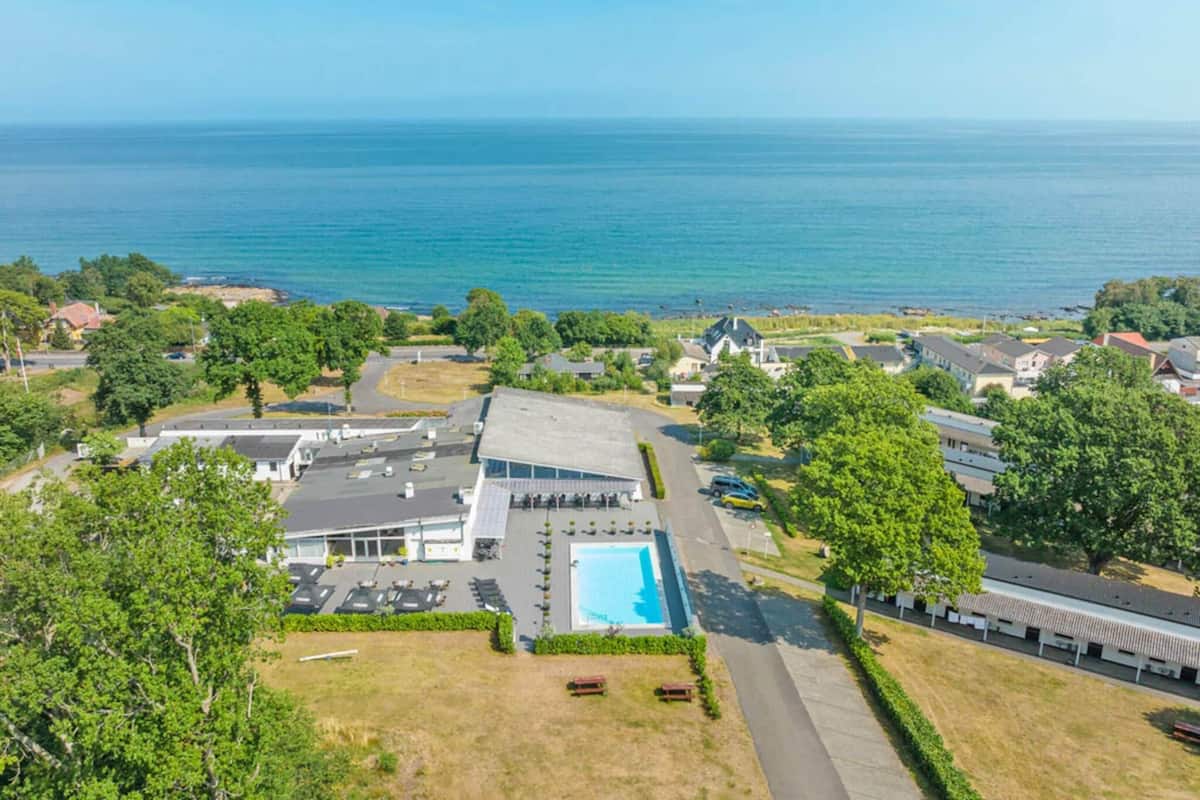 An aerial view of a coastal property with a swimming pool, multiple buildings, and a clear view of the ocean.