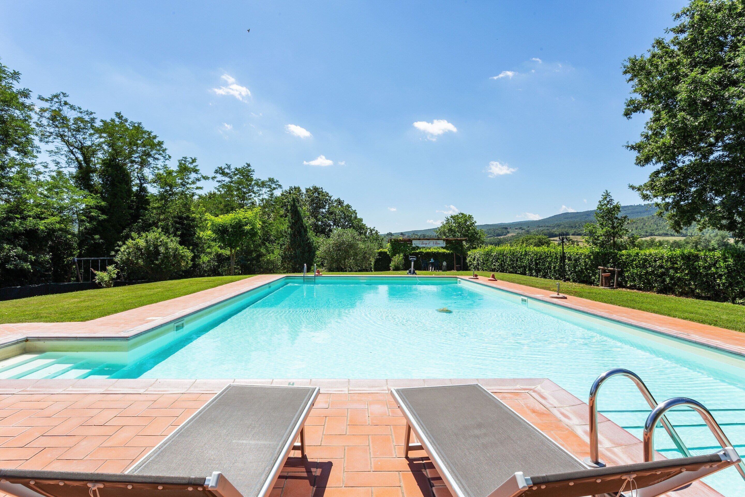 Una piscina rectangular amb dues gandules i una escala, envoltada per un jardí ben cuidat i arbres.