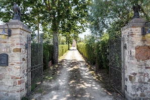 A pathway leading to a gated area with stone walls, metal gates, and a statue. - Scenic Apartment in Casole D'elsa With Pool (Casole d'Elsa)