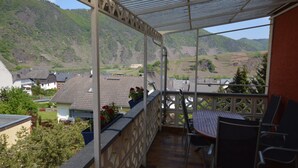 A balcony with a table and chairs, overlooking a valley with houses and hills. - Comfortable Holiday Home Near Vineyards in Bremm (Bremm)