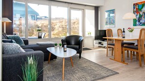 A modern living room with a sofa, coffee table, and dining area. - 4 Person Holiday Home on a Holiday Park in Ringkobing (Ringkobing)