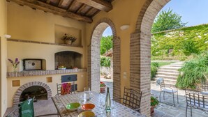 Eine Terrasse im Freien mit einem Backofen aus Ziegeln, einem Esstisch und Blick auf den Garten.