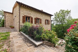 A stone building with a balcony, potted plants, and a garden.