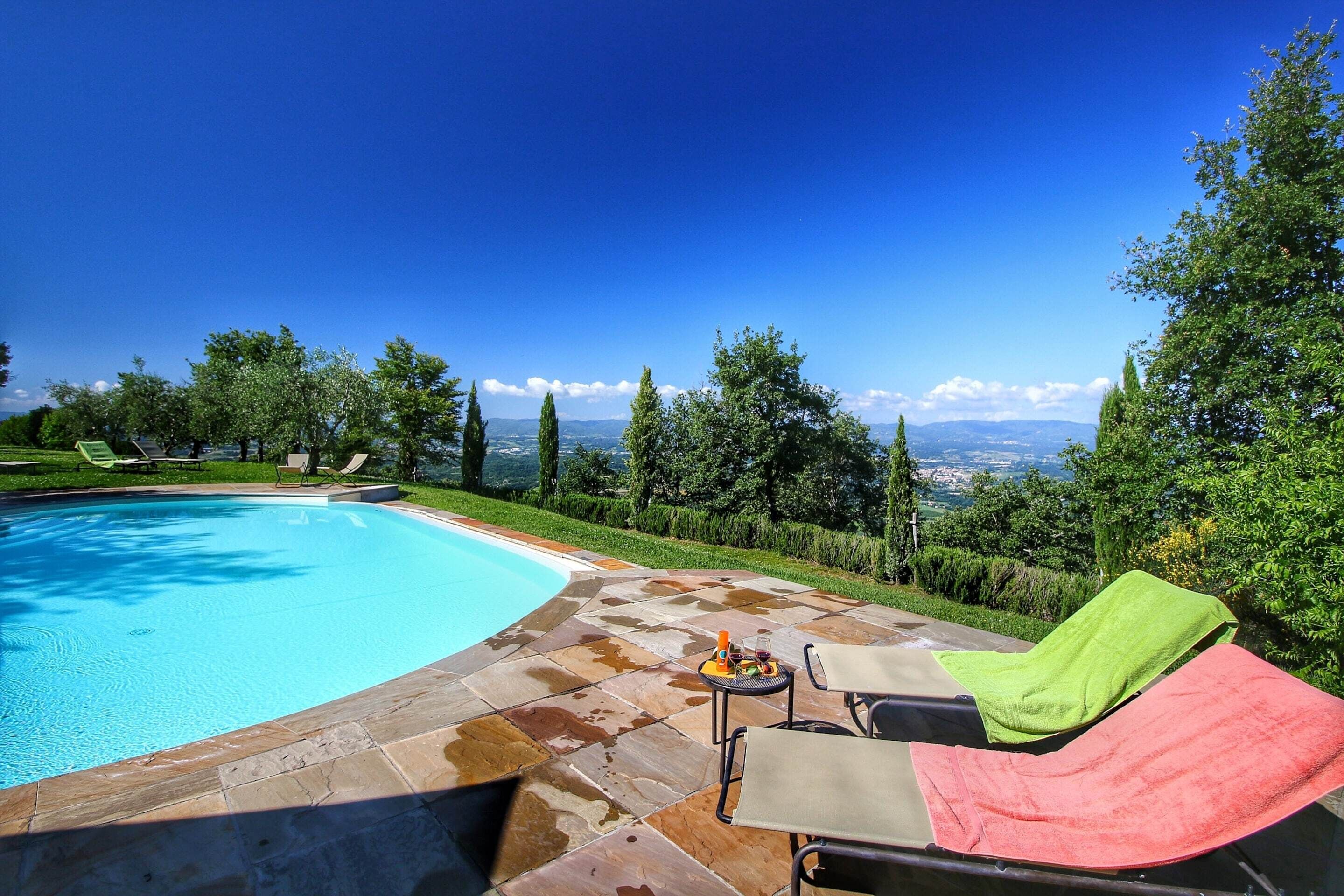 A swimming pool with a tiled deck, lounge chairs, and a view of the landscape.