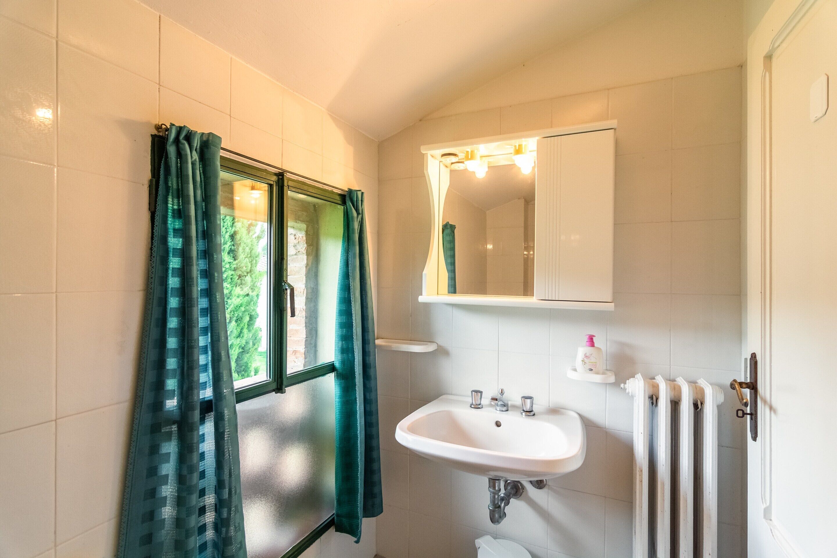 Un bagno con un lavandino bianco, uno specchio e una finestra con tende.