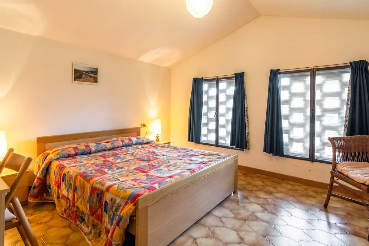 Een slaapkamer met een houten bed, een stoel, een bureau en een raam met gordijnen.