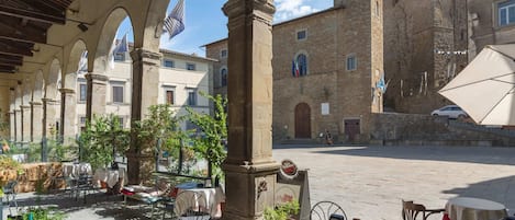 An outdoor café area with stone arches, tables, and chairs, surrounded by historic buildings.