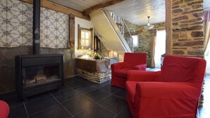 A cozy living room with a stone fireplace, red chairs, and a wooden staircase. - Beautiful Holiday Home in Belgium (Bertrix)