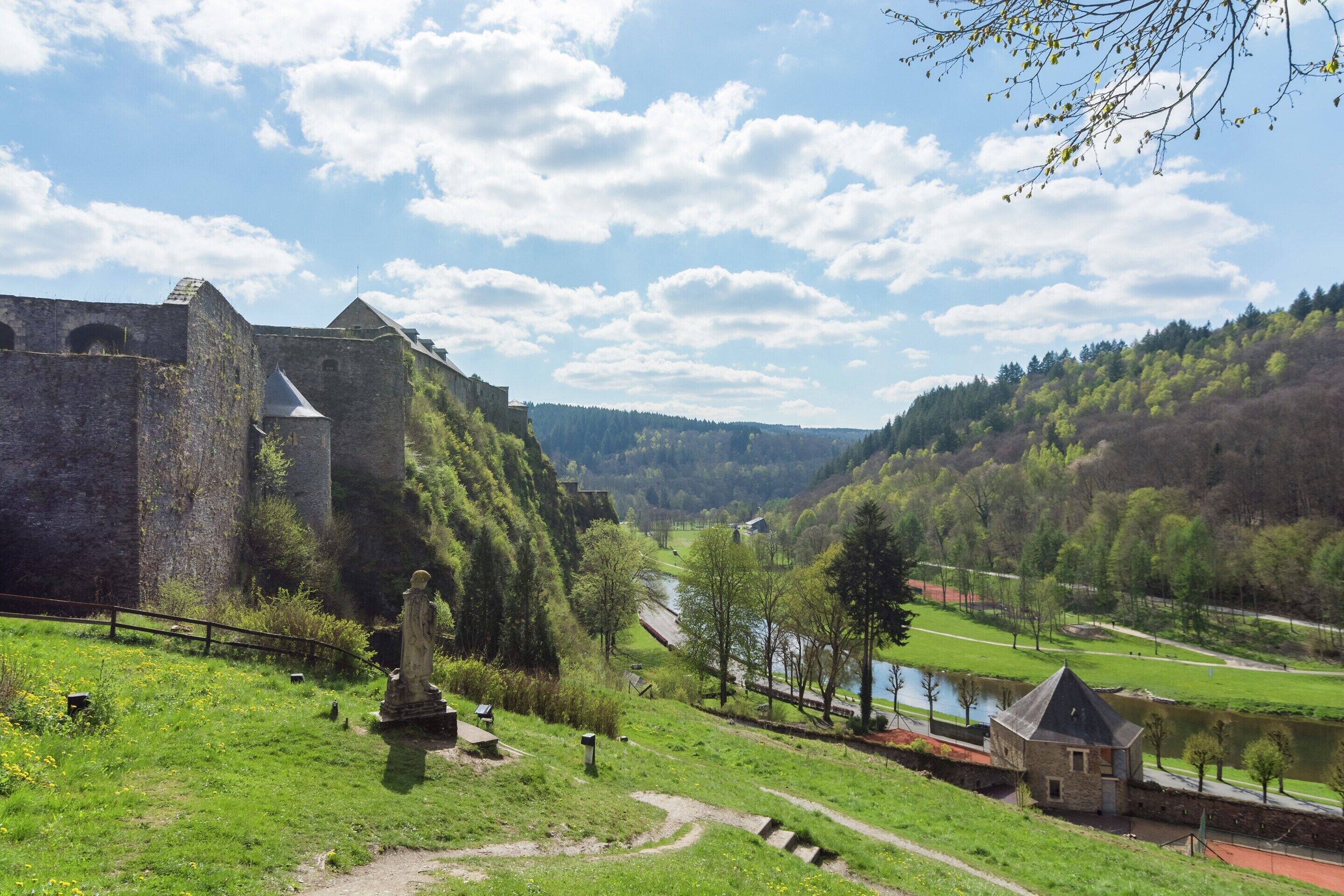 Ein historisches Steinhaus mit einem Turm, umgeben von üppiger Vegetation und einem Fluss.